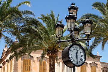 Fototapeta na wymiar Round clock on a lamppost on the Plaza de Alfonso III or Plaza de las palmeras in Ciutadella de Menorca.