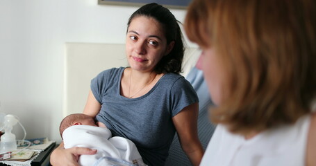 Friends in conversation about maternity parent holding newborn baby speaking to female friend