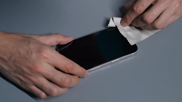 Close-up of unrecognizable repairman squeezing air out after installing safety glass on modern mobile phone. Step-by-step guide to replacing broken protective glass on smartphone, slow motion.