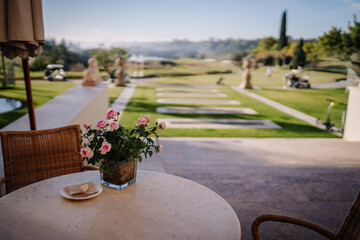 Sotogrante, Spain - January 26, 2024 -  table with a vase of pink roses overlooking a landscaped garden and golf course.