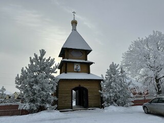 wooden bell tower against a background of snow-covered trees. Kazan Alexievo-Sergievskaya hermitage. Penza region Russia