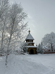 wooden bell tower against a background of snow-covered trees. Kazan Alexievo-Sergievskaya hermitage. Penza region Russia