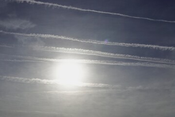 Multiple condensation trails cross in the blue sky covering the sun.