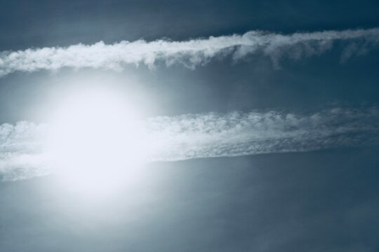 Multiple condensation trails cross in the blue sky covering the sun.