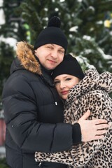 Fototapeta premium Love romantic couple lovestory. Man hugging woman, kissing girl in Christmas winter fur trees decoration. Romantic date. Walking,having fun. Stylish clothes,fur leopard print coat, black jacket, hat