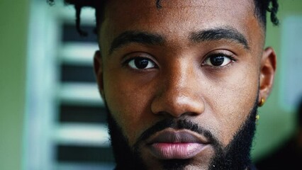 Portrait of a black young man staring at camera with solemn serious expression, close-up facial features of a person of African descent in 20s