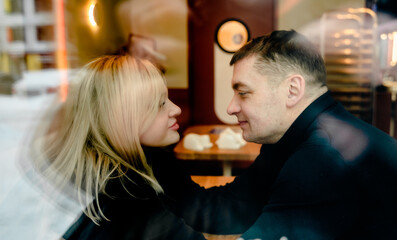 Love romantic couple lovestory. Man hugging woman, kissing blonde girl in cozy coffee shop cafe. Romantic family date. Sitting at window table in restaurant. Intimate romance atmosphere