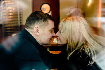Love romantic couple lovestory. Man hugging woman, kissing blonde girl in cozy coffee shop cafe. Romantic family date. Sitting at window table in restaurant. Intimate romance atmosphere