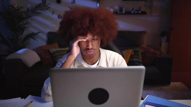 Front view of an overwhelm young African american male studying late from home using a laptop, typing frustrated by not understanding the online class.