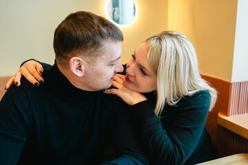 Love romantic couple lovestory. Man hugging woman, kissing blonde girl in cozy coffee shop cafe. Romantic family date. Sitting at window table in restaurant. Intimate romance atmosphere