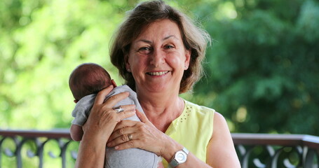 Portrait of grand mother holding newborn baby grand-son looking to camera smiling