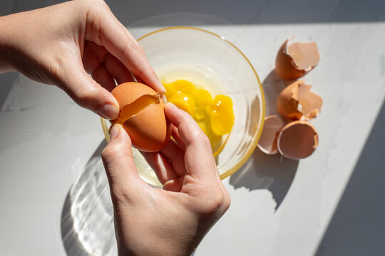 Hands Cracking Brown Egg Over Glass Bowl in Kitchen