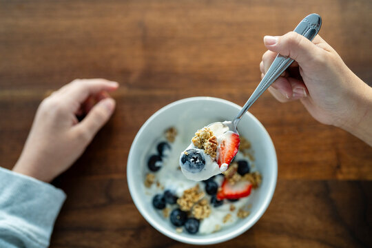 Person Enjoying Spoonful of Yogurt, Granola, and Fruit for Breakfast