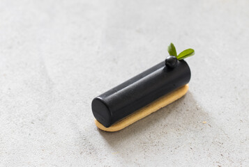 Modern dessert. Black matcha cream cake cylindrical shape, bar on cookie.  Light grey background. Close up
