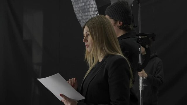 The crew backstage. Woman director with script, cameraman with camera and man lighting in the studio during filming. A woman nods her head approvingly, satisfied with the filming.