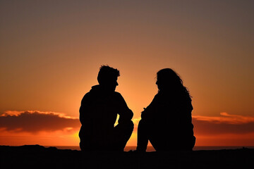 Silhouette man and woman sitting against a dramatic sunset