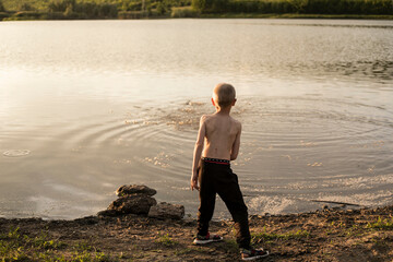 Fototapeta na wymiar Rear view of a boy throwing stones into a lake.