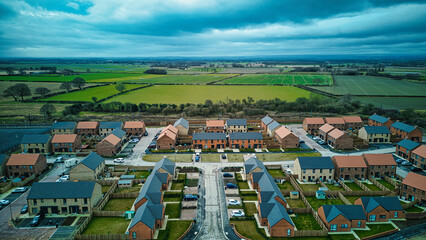Aerial view of a modern residential housing development amidst green fields under a cloudy sky.
