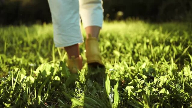 Gardener female person feet in yellow rubber boots walks on green grass and rubble land road ground. Autumn season. Close-up. 