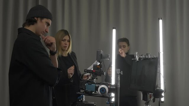 Female producer, camera operator and lighting technician in the studio during filming. The lighting technician adjusts the lighting, and the producer and cameraman discuss the shooting plan.