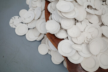 A pile of white, unfinished ceramic plates at various stages of the manufacturing process,...