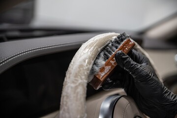 Car wash employee or a car detailing studio thoroughly cleans a light leather steering wheel with a...