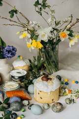 Happy Easter! Stylish easter natural dyed eggs, meat, bread, butter, beets, basket and flowers on rustic table. Traditional easter orthodox holiday food for blessing and daffodils bouquet