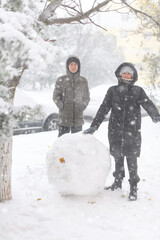 a girl and boy is playing with snow on the street, making snowman, it is snowing, a blizzard and frost on a winter day