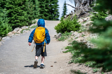 young child wearing a backpack and jacket on a hike up a dusty trail.  - obrazy, fototapety, plakaty