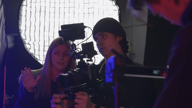 The producer, videographer and lighting technician prepare for filming. A female producer gives instructions to the cameraman and lighting technician. Videographer shows thumbs up.
