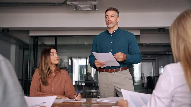 Mature executive manager leading group meeting with business team. Older Latin company executive planning strategy discussing financial report with diverse people in office working consulting clients.