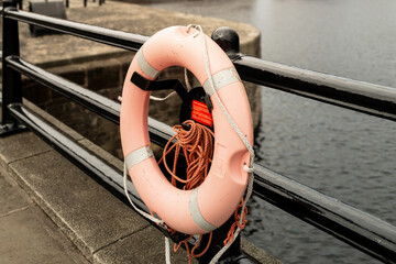 Liverpool, UK - October 10 2023 : a lifesaving ring buoy in weathered orange against black steel and chain railings by the water and red brick