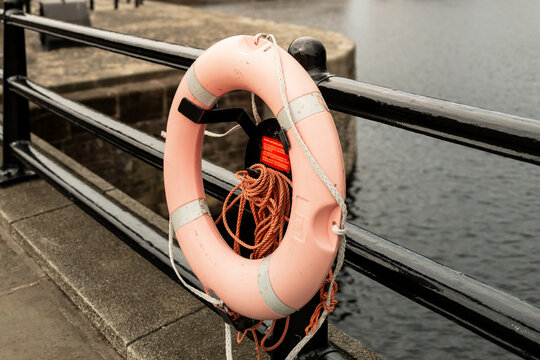 Liverpool, UK - October 10 2023 : a lifesaving ring buoy in weathered orange against black steel and chain railings by the water and red brick