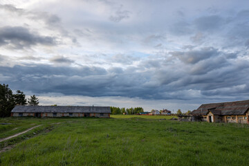 Fototapeta premium Rural landscape with an old cowshed in the background of a landscape with clouds. abandoned mission