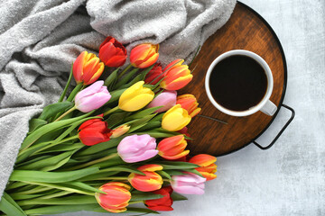 Colorful bouquet of tulips and a cup of coffee or hot tea on a tray - cozy hygge spring background