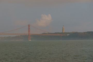 Red bridge 25 de Abril Bridge and statue of Cristo Rei during a slightly misty day, Lisbon, Portugal