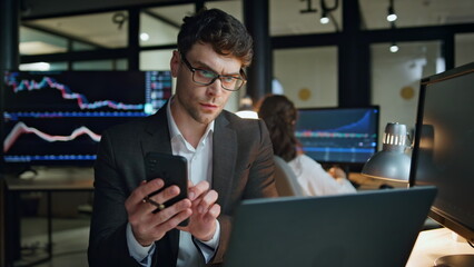 Stock trader holding smartphone work in office. Focused man professional check - obrazy, fototapety, plakaty