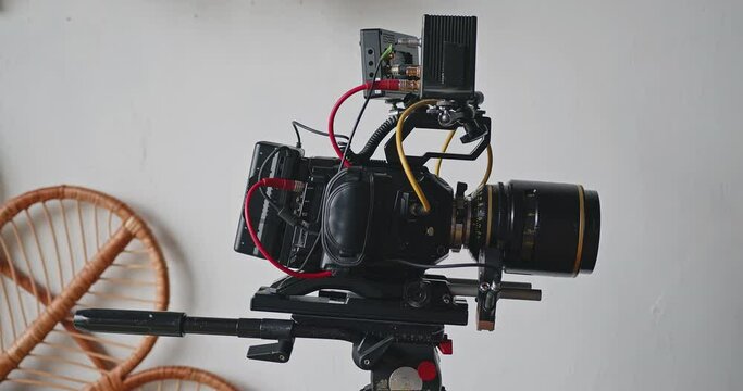 A movie camera with cinema equipment on a tripod stands in a white room