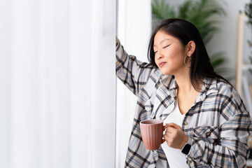 Chinese happy woman in a daydreaming at home enjoying coffee in the morning