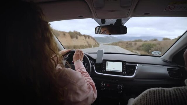 Slow motion of Caucasian woman driver and African American girl co-driver enjoying music on road trip. Multiracial young people on vacation singing and dancing in car. Friendship relations on holiday.