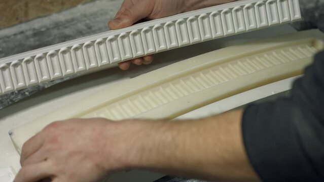 Close up molding a gypsum cornice. Mans hands holding silicone mold for producing cornice. Production of luxury frames.