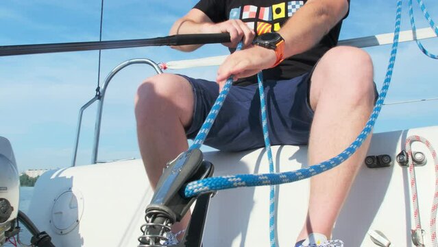 Man with force pulls rope sitting on sailboat deck. Experienced traveler controls position of mainsail pulling ropes going downwind