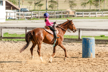 A girl practicing riding a beautiful horse in the racing sport past barrels on a ranch across the...