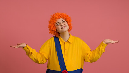 a cheerful clown in a wig and a yellow-blue suit spread her arms to the sides on a colored background