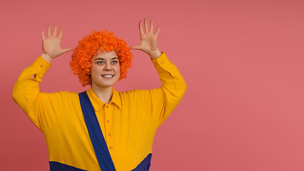 cheerful smiling clown in a wig and a yellow-blue suit raised up his hands and shows empty palms on a colored background with copy space