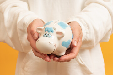 A hand inserting a coin into a cow-painted piggy bank