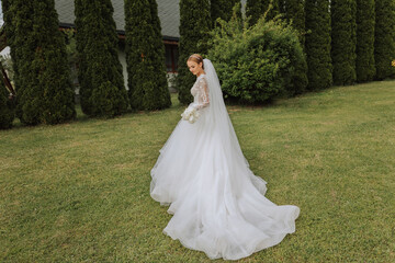 Photo from the back. A beautiful young woman in a white wedding dress is smiling on a warm wedding summer day