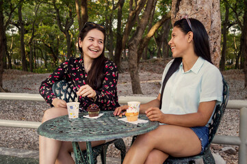 Two young girls outdoors chatting and laughing. Friends having fun sitting in a park.