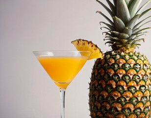 A glass of pineapple juice cocktail stands next to an annas fruit on a white background