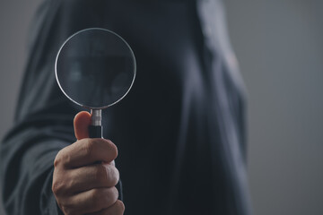 man hand holding magnifying glass on grey background, closeup.search and Find keywords concept. research quality tool. 